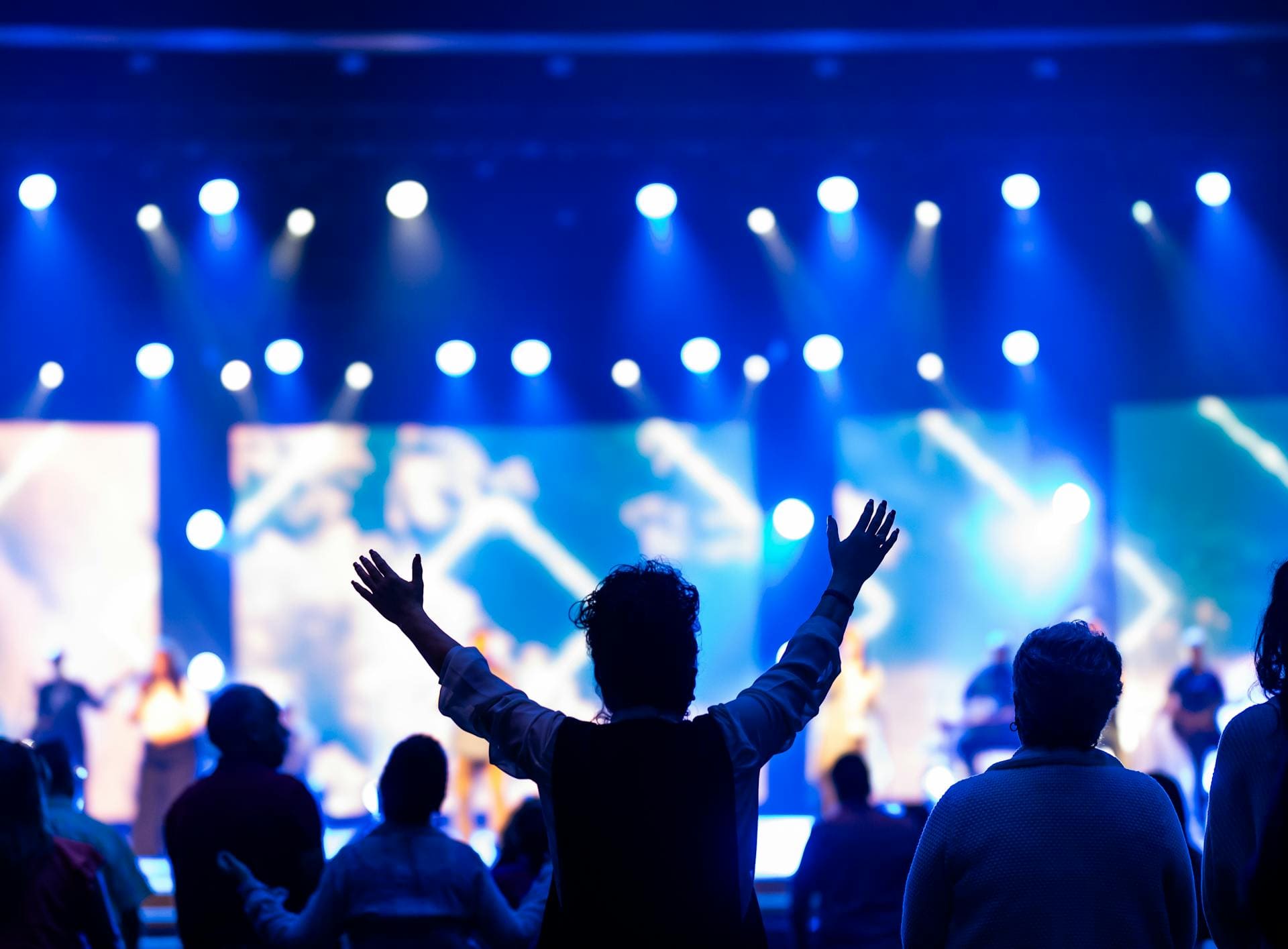 Público en un concierto o espectáculo, con los brazos levantados y luces azules en el escenario